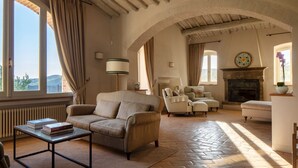 A spacious living room with a fireplace, comfortable seating, and large windows offering a view. - Casolare di Rietine, Gaiole in Chianti, Siena and Chianti (Gaiole in Chianti)