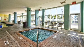 A pool area with a hot tub, lounge chairs, and a view of palm trees outside. - 🌴Stunning Ocean Views | Pools + Hot Tub | Bay View Resort 1004B🌴 (Myrtle Beach)