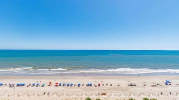 A beach with umbrellas and people, a clear sky, and the ocean.