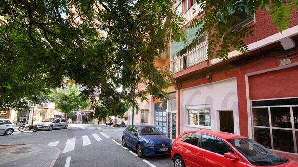 Une vue de rue avec des voitures garées, un passage piéton et des immeubles dotés de balcons et d’auvents.