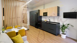 Une cuisine moderne équipée d’un four à micro-ondes, d’un réfrigérateur et d’un évier. On y trouve une table à manger avec des chaises et une plante.