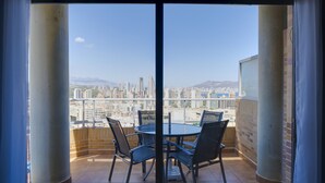A balcony with a round table and four chairs, overlooking a cityscape with tall buildings and mountains in the distance.