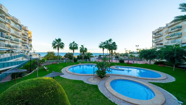 A resort with multiple swimming pools, palm trees, and a view of the sea. - AL Piso de 2 dormitorios en El Campello (El Campello)