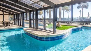 A swimming pool with a glass enclosure, outdoor seating, and a view of palm trees. - 💎Oceanfront~Lazy River~Awesome Amenities~Breakers Resort 1870💎 (Myrtle Beach)