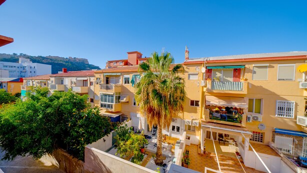 Un edificio residencial con balcones, un patio con palmeras y vistas del entorno.