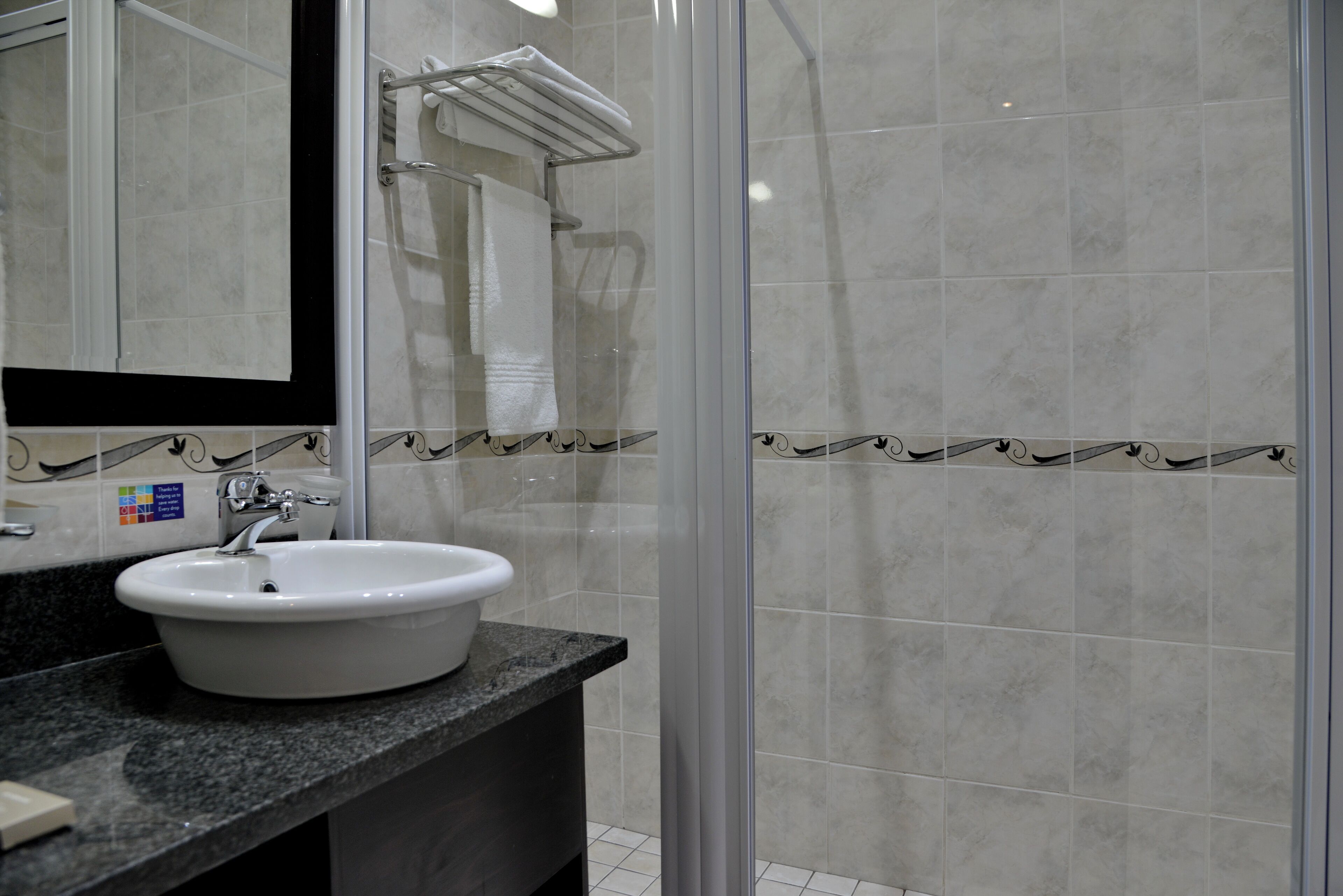 A modern bathroom with a white sink, a glass shower enclosure, and a marble-tiled wall.