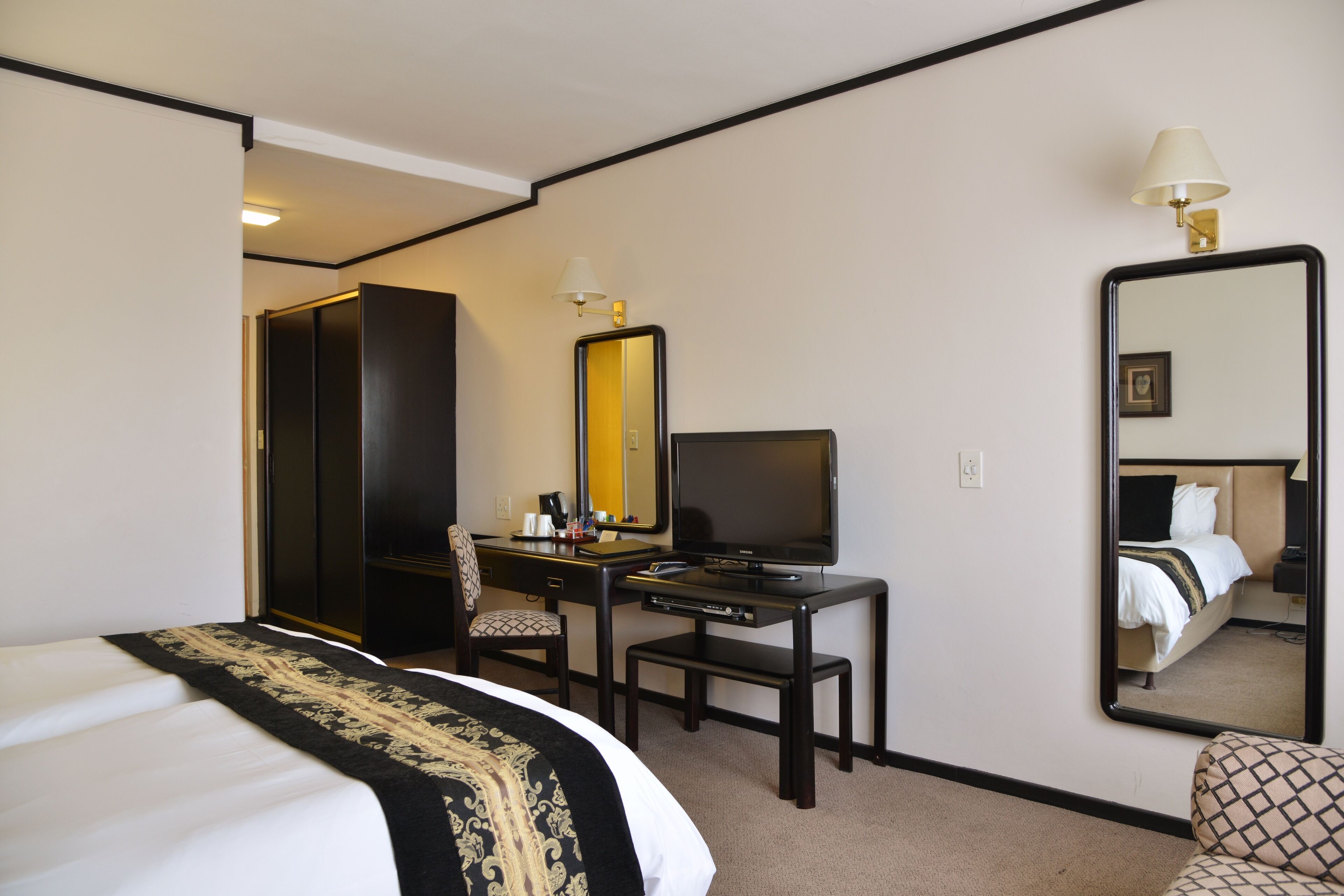Habitación de hotel con cama, escritorio con televisor, silla, lámpara de escritorio y un espejo grande.