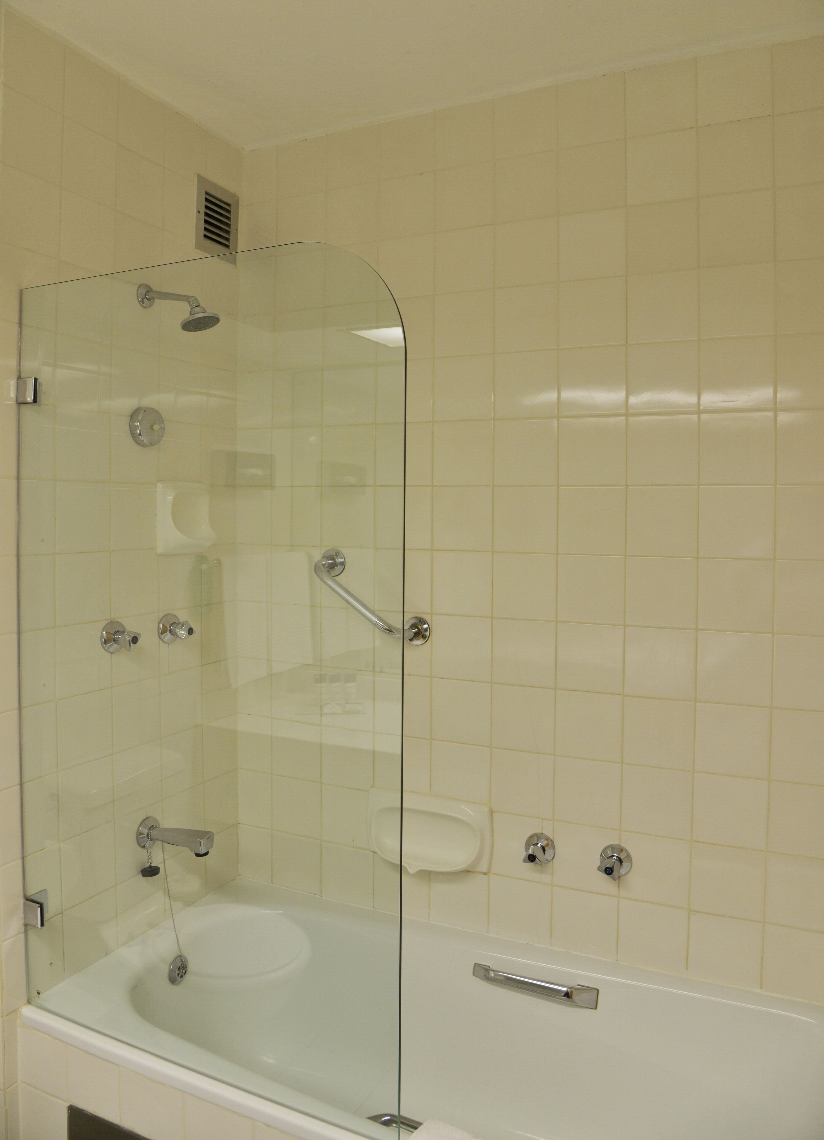 Cabina de ducha con paredes de cristal, bañera, inodoro y barra de apoyo.