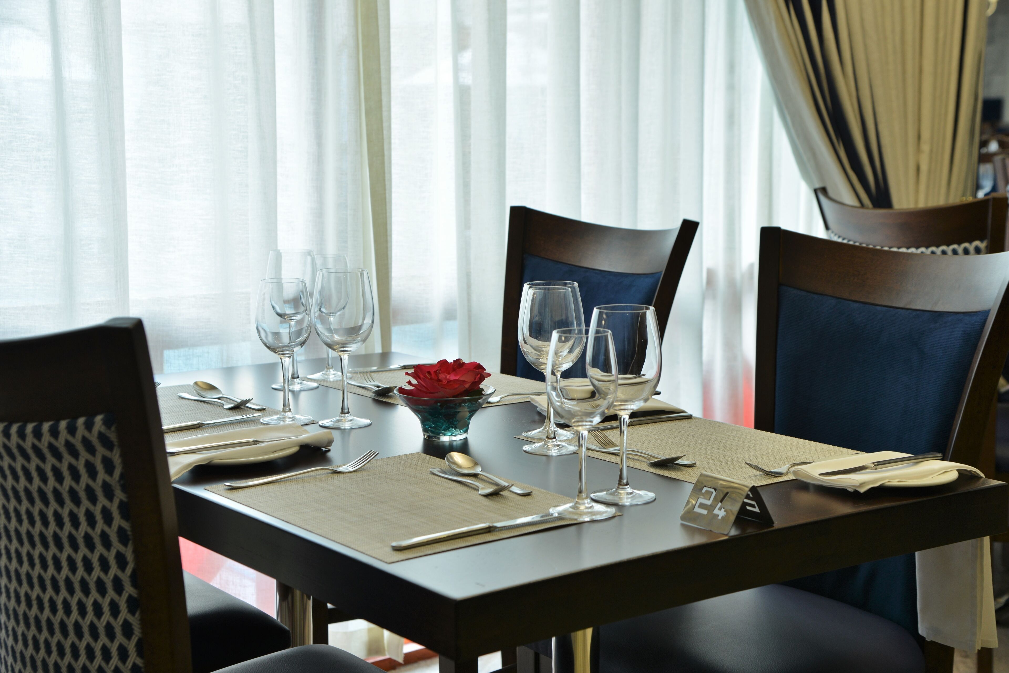 A dining table set with wine glasses, cutlery, and a red flower centerpiece.
