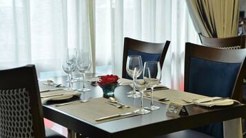 A dining table set with wine glasses, cutlery, and a red flower centerpiece.