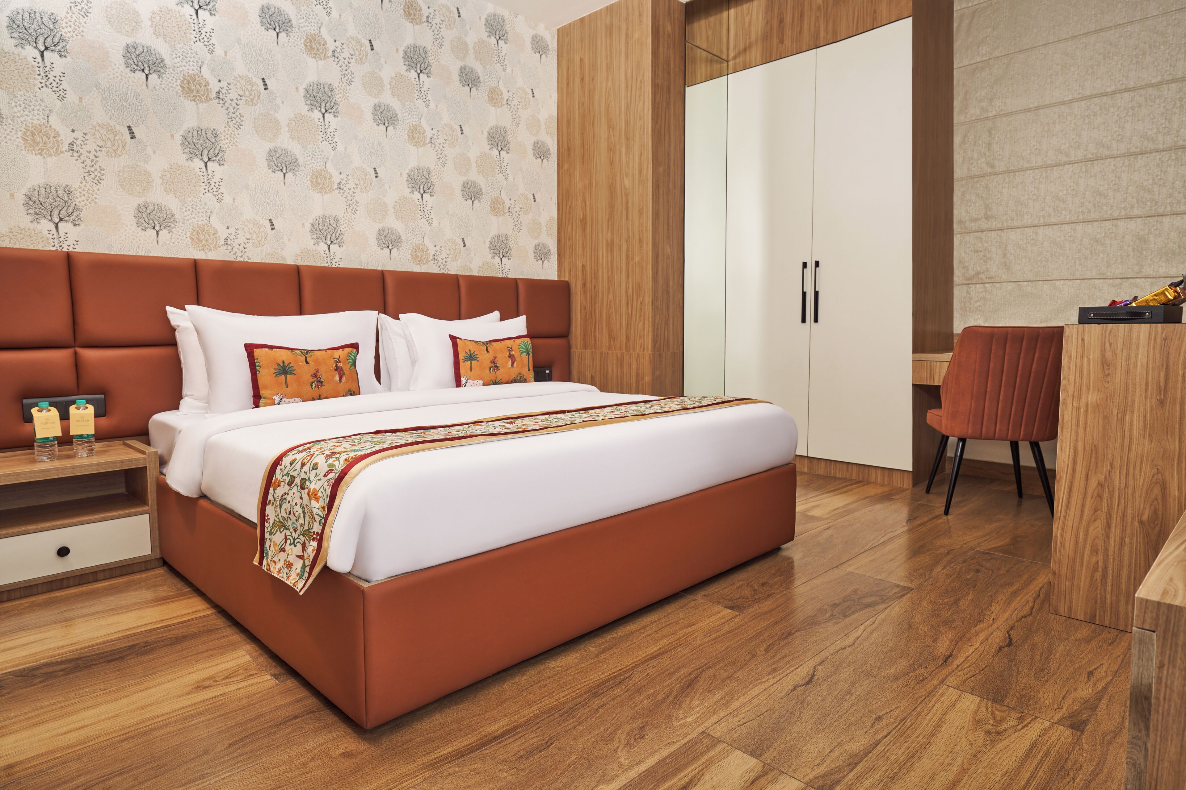 Una habitación de hotel moderna con una cama grande, suelo de madera, un armario y un escritorio con silla.