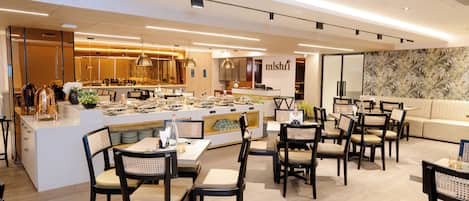 Un restaurante moderno con una isla central, varias mesas y sillas.
