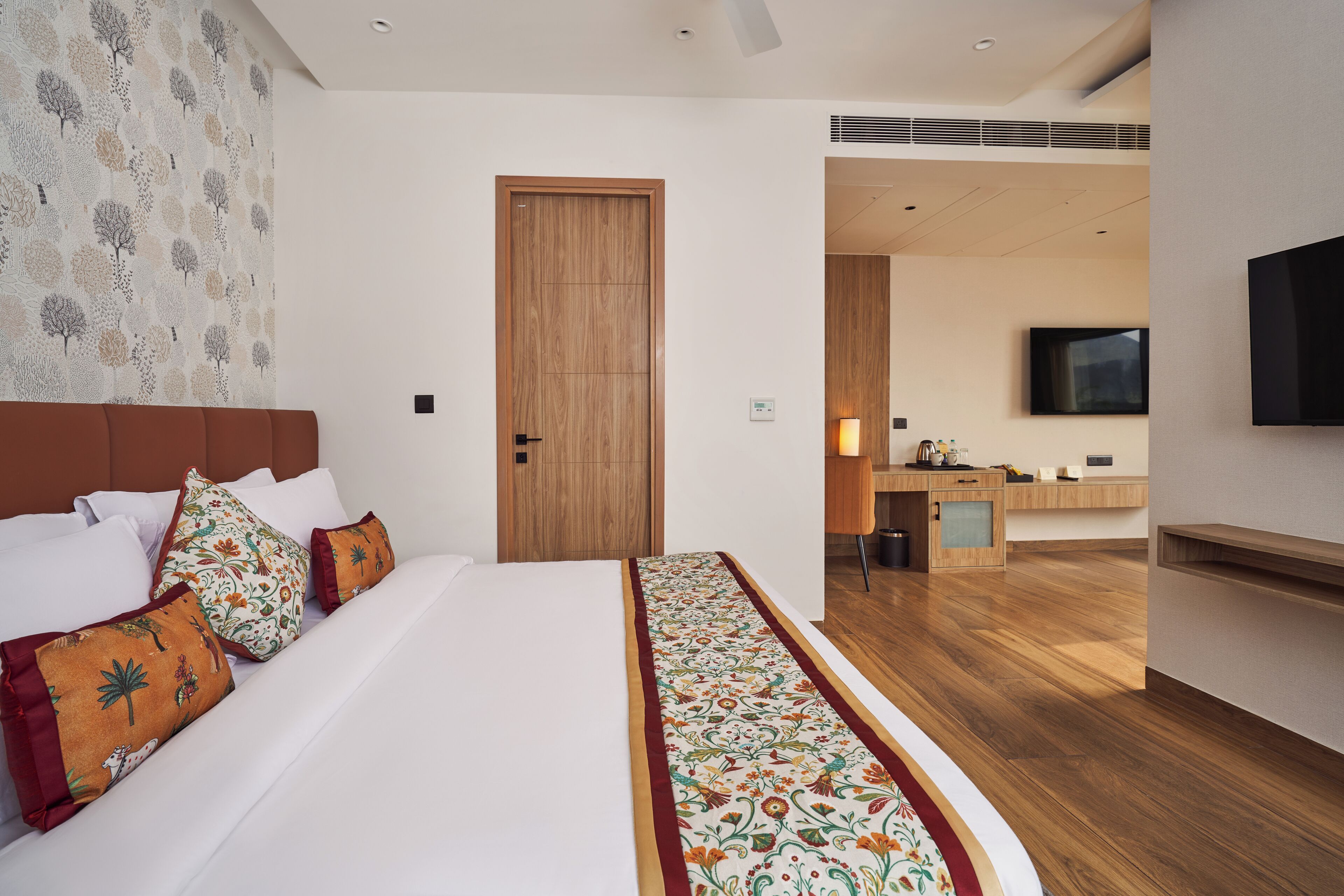 A hotel room with a large bed, a wooden door, a TV, and a desk area.