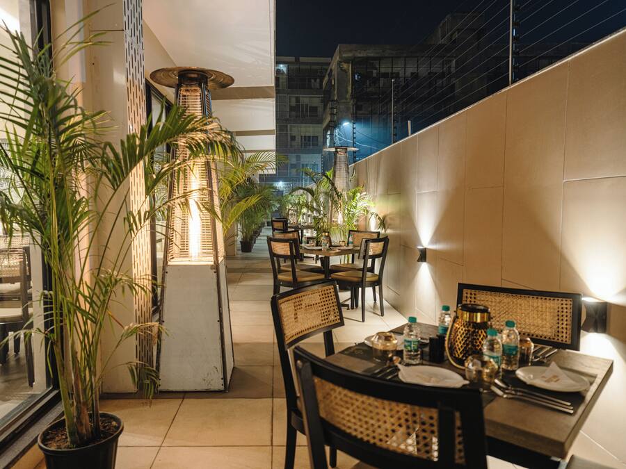 Un espace de restauration en plein air, avec des tables et des chaises, des plantes en pot et une haute colonne illuminée.