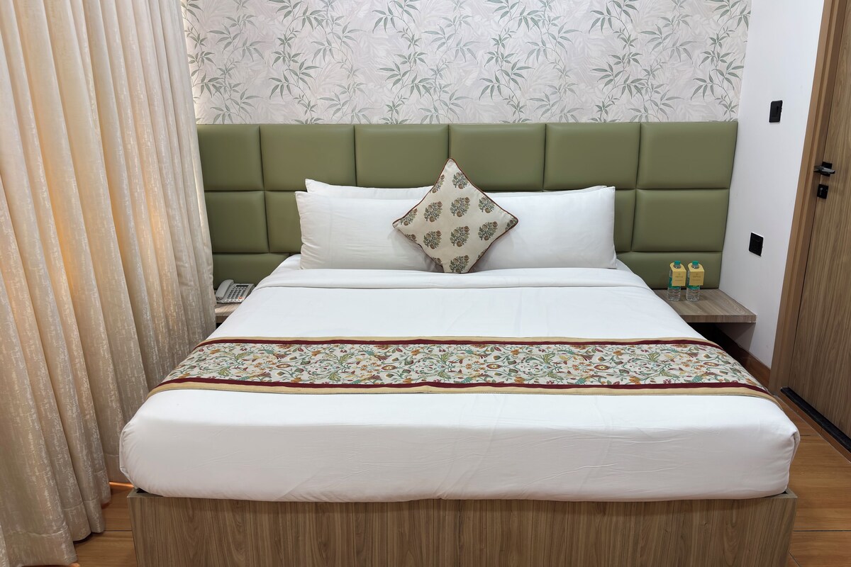 A neatly made bed with a green headboard, a patterned bedspread, and two bottles on a nightstand.