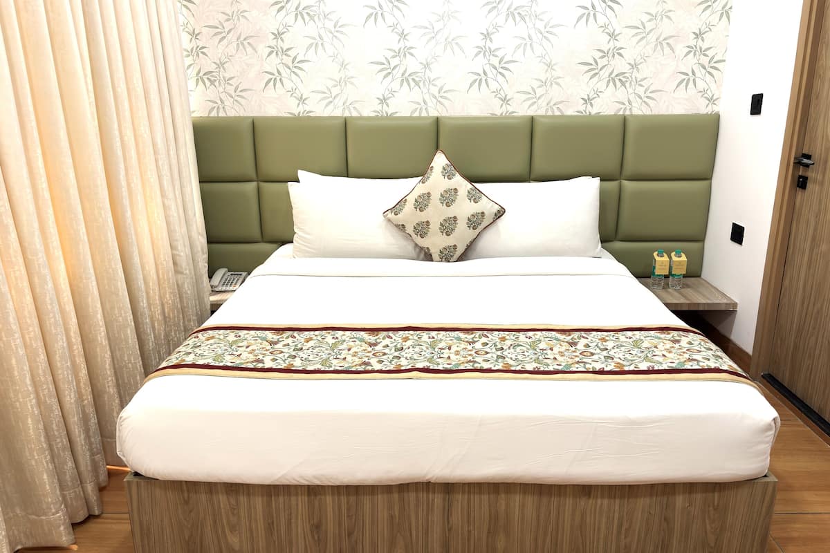 A hotel room with a bed, a nightstand, a wooden headboard, a patterned bedspread, and a floral wallpaper.
