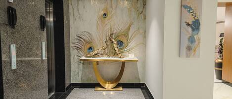 A lobby with a marble floor, a gold table centerpiece, and a peacock feather mural.