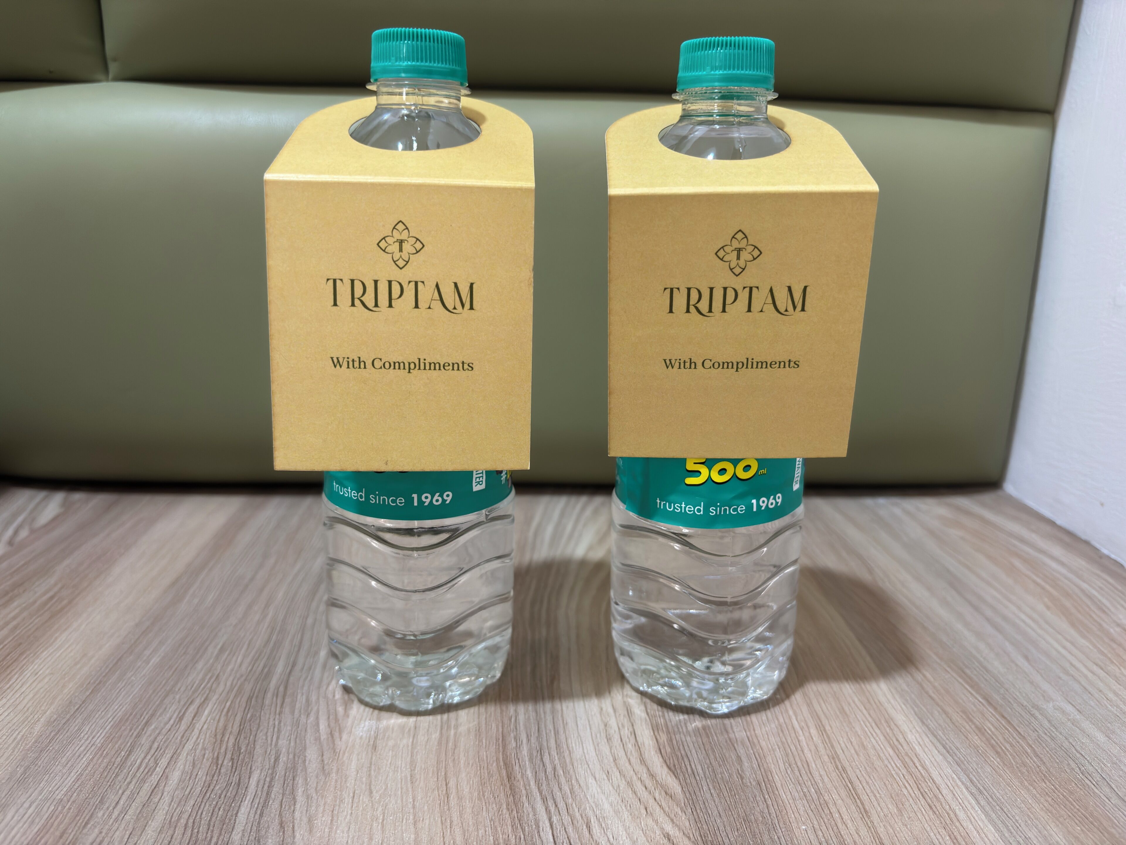 Two TRIPTAM water bottles with cardboard boxes labeled 'TRIPTAM With Compliments' and '500ml' on a wooden surface.