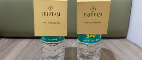 Deux bouteilles d’eau TRIPTAM, accompagnées de leurs emballages en carton portant les inscriptions « TRIPTAM, avec nos meilleurs vœux » et « 500 ml », sont posées sur une surface en bois.