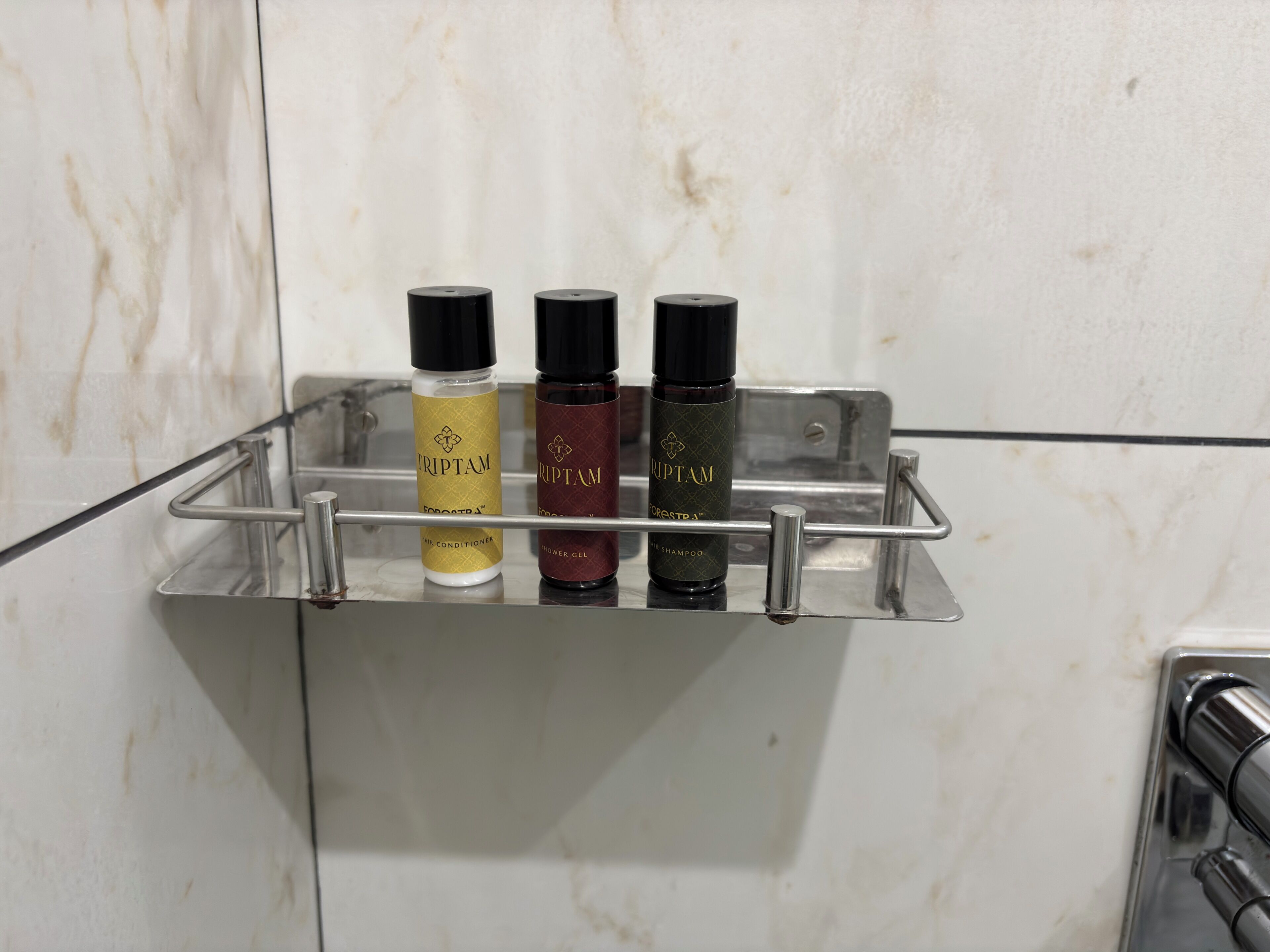 Un estante en el baño con tres botellas de productos capilares Triptam.
