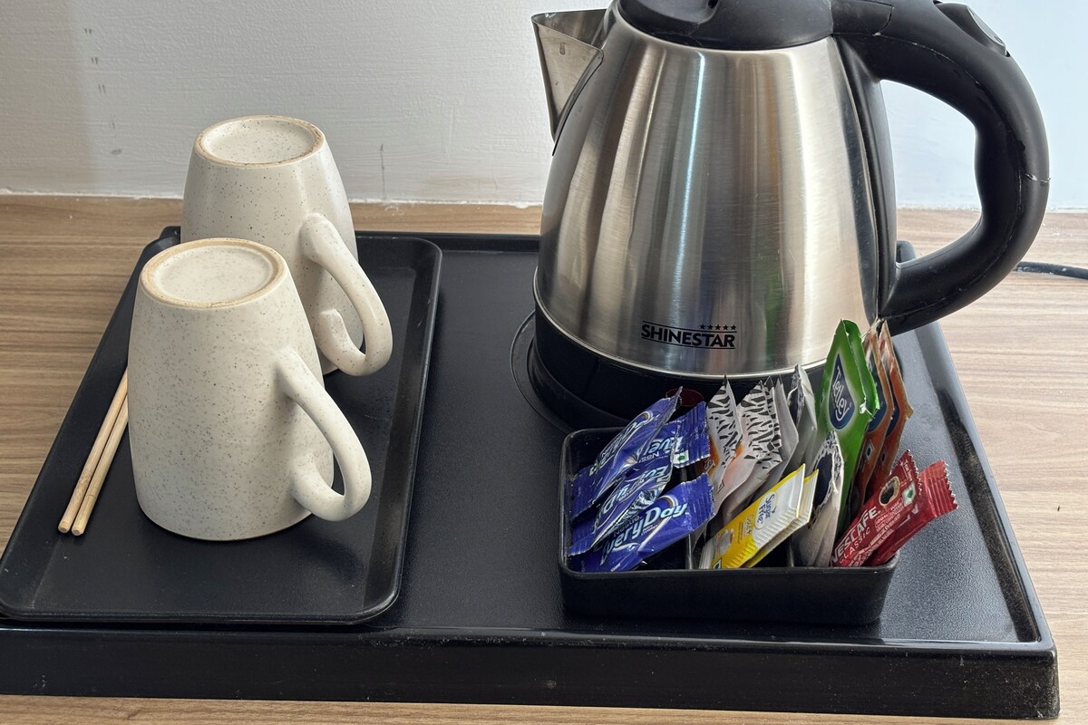 A tray with two ceramic cups, a stainless steel kettle, and a packet holder with tea bags.