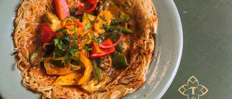 Un plato de fideos con verduras y carne, decorado con hierbas.