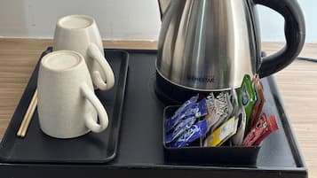 Una bandeja con dos tazas de cerámica, una tetera de acero inoxidable y un soporte para bolsitas de té.