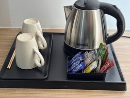 Una bandeja con dos tazas de cerámica, una tetera de acero inoxidable y un soporte para bolsitas de té.