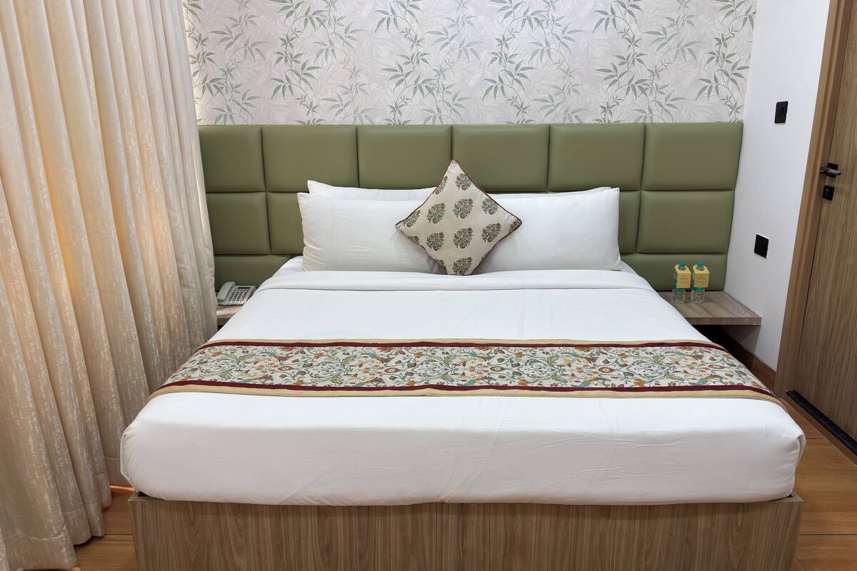 A neatly made bed with a green headboard, a patterned bedspread, and two bottles on a nightstand.