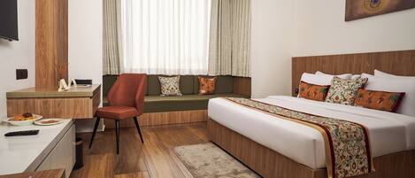 A hotel room with a bed, a desk, a chair, a window with curtains, and a wall-mounted TV.