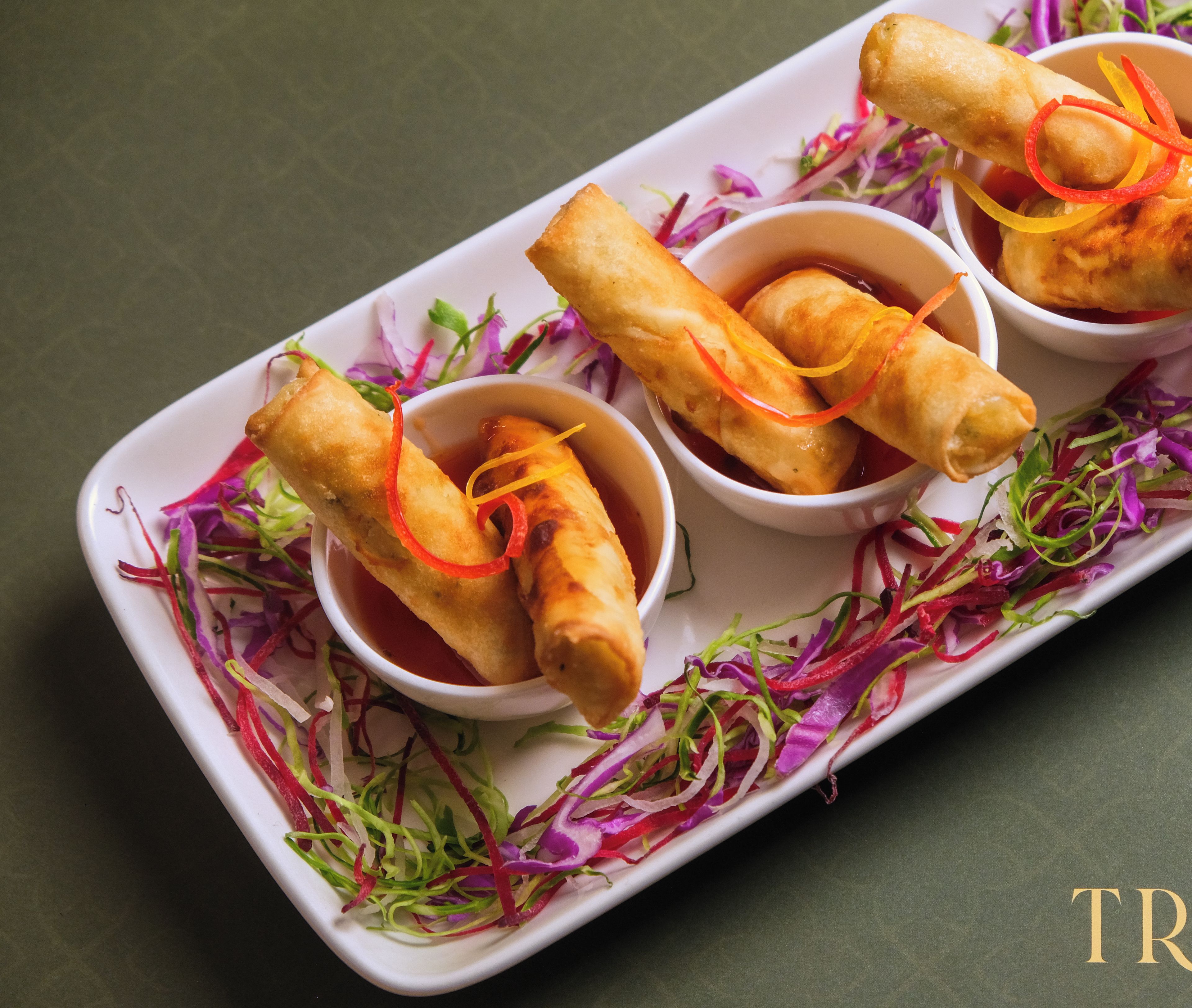 A tray of spring rolls with dipping sauce and shredded vegetables.