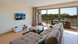 Een moderne woonkamer met een grote bank, een flatscreen televisie, een salontafel en een balkon met een tafel en stoelen.