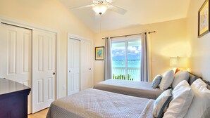 A bedroom with two beds, a ceiling fan, a view of the ocean, and a door. - Sleep 16 guests over two side-by-side homes in exclusive Key Cove Landings (Key West)