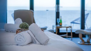 Una habitación de hotel con cama, una silla, una mesita con una botella y vista al mar.