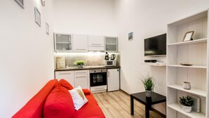 A compact living space with a kitchenette, a red sofa, a small black table, and a white shelving unit. - Stay close to Day Night HOT SPOT Nightlife (Budapest)
