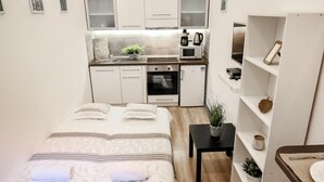A compact hotel room with a bed, a small desk, a kitchenette, and a shelf with decorative items. - Stay close to Day Night HOT SPOT Nightlife (Budapest)