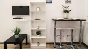 A modern living room with a flat-screen TV, a white shelving unit, a small table with two bar stools, and a potted plant. - Stay close to Day Night HOT SPOT Nightlife (Budapest)