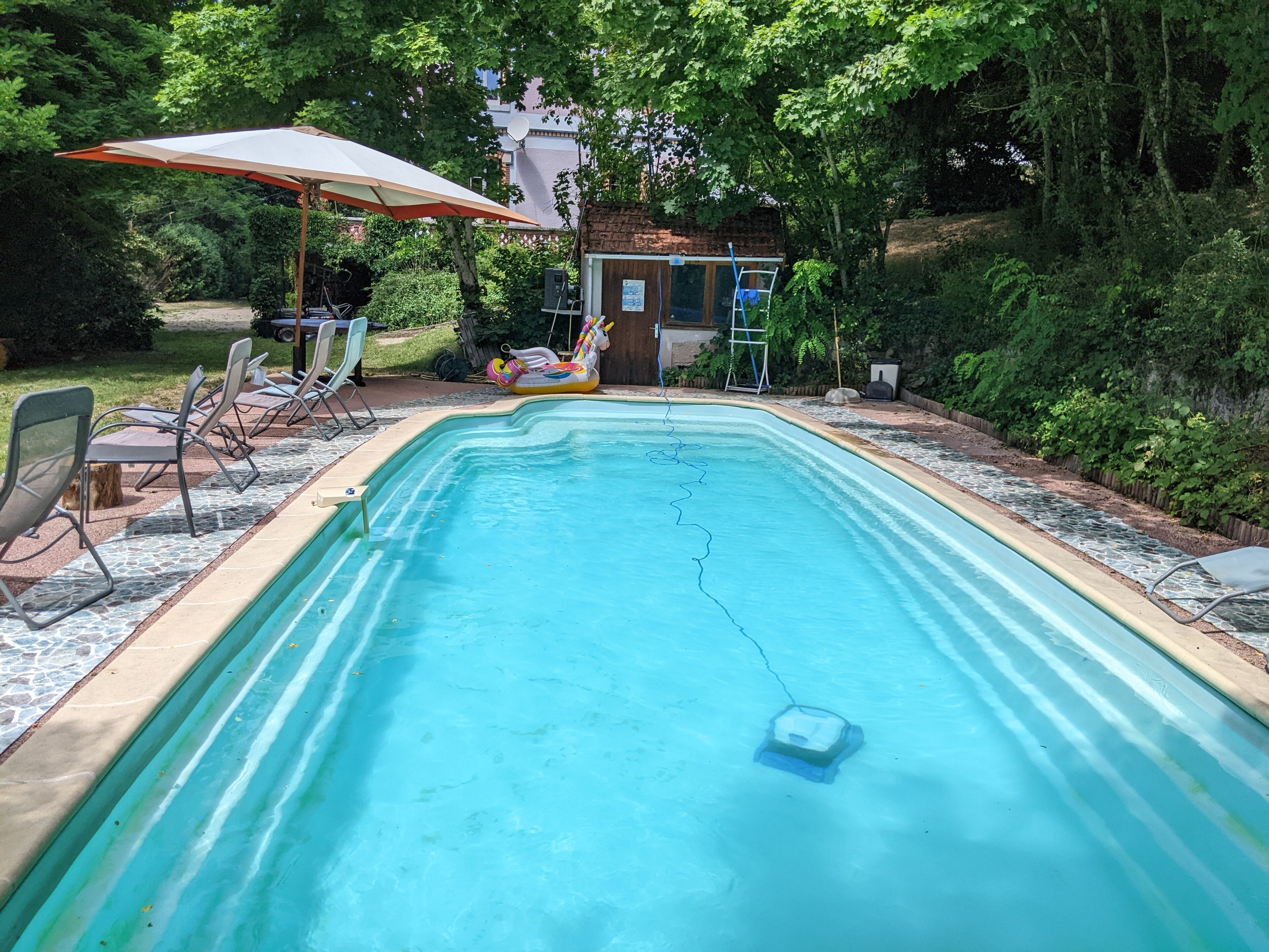 A rectangular swimming pool with a tiled deck, surrounded by lounge chairs and an umbrella.