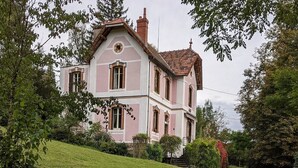 A two-story house with a pink and white facade, a tiled roof, and a front entrance with a small porch.
