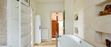 A modern bathroom with a freestanding bathtub, a white radiator, and a tiled floor.