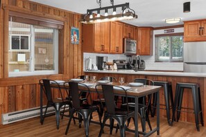 A kitchen with wooden cabinets, a central island with bar stools, and a window with blinds. - Family friendly 2 bedroom cabin themed interior (Winter Park)