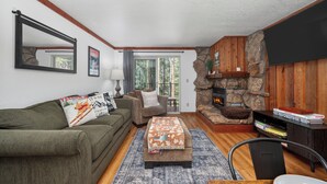 A living room with a stone fireplace, a couch, a coffee table, and a television. - Beaver Village Unit #1514 Family friendly 2 bedroom cabin themed interior (Winter Park)