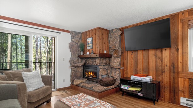 A living room with a stone fireplace, a flat-screen TV mounted on the wall, a sofa, and a coffee table. - Beaver Village Unit #1514 Family friendly 2 bedroom cabin themed interior (Winter Park)