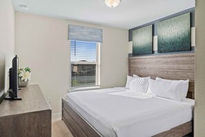 Ein Schlafzimmer mit einem Bett, einem Fernseher, einem Fenster mit Jalousien und Bildern an der Wand.