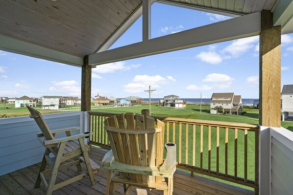 Una terraza de madera con dos sillas Adirondack, una mesita y vistas a un campo de golf y al océano.