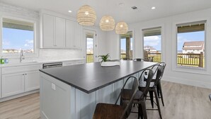 A modern kitchen with white cabinets, a large island, pendant lights, and large windows with a view of the backyard.