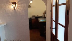 En hall med ett klinkergolv, en väggmonterad lampa och en trädörr med glaspaneler.