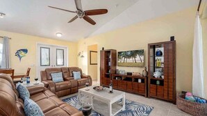 A living room with a brown leather sofa, a white coffee table, and a ceiling fan. - Kings Castle - 3BR w/ Bikes & Boat Dock Access (Cape Coral)