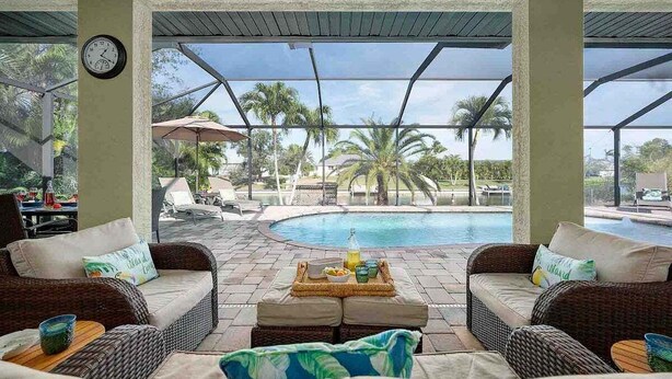 A covered outdoor seating area with wicker furniture and a pool view. - Kings Castle - 3BR w/ Bikes & Boat Dock Access (Cape Coral)
