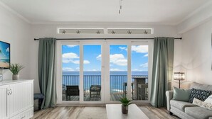 Een woonkamer met uitzicht op de oceaan, een witte bank, een salontafel en een televisie op een kast.